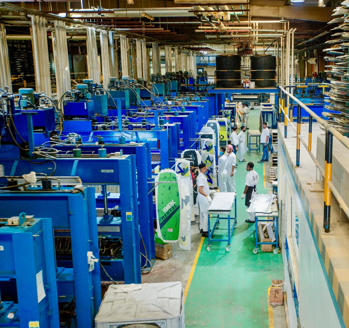 Workers alongside blue machinery and racks of sports boards in an SWS factory image.
